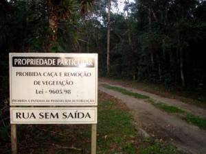 Placa em propriedade particular no município de Cananéia, avisando que é proibida a caça e remoção de vegetação. A vegetação presente na foto é uma floresta de restinga alta.